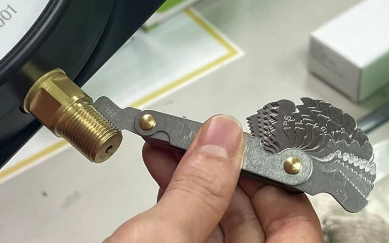 Technician checking instrument fitting thread pitch with a thread gauge