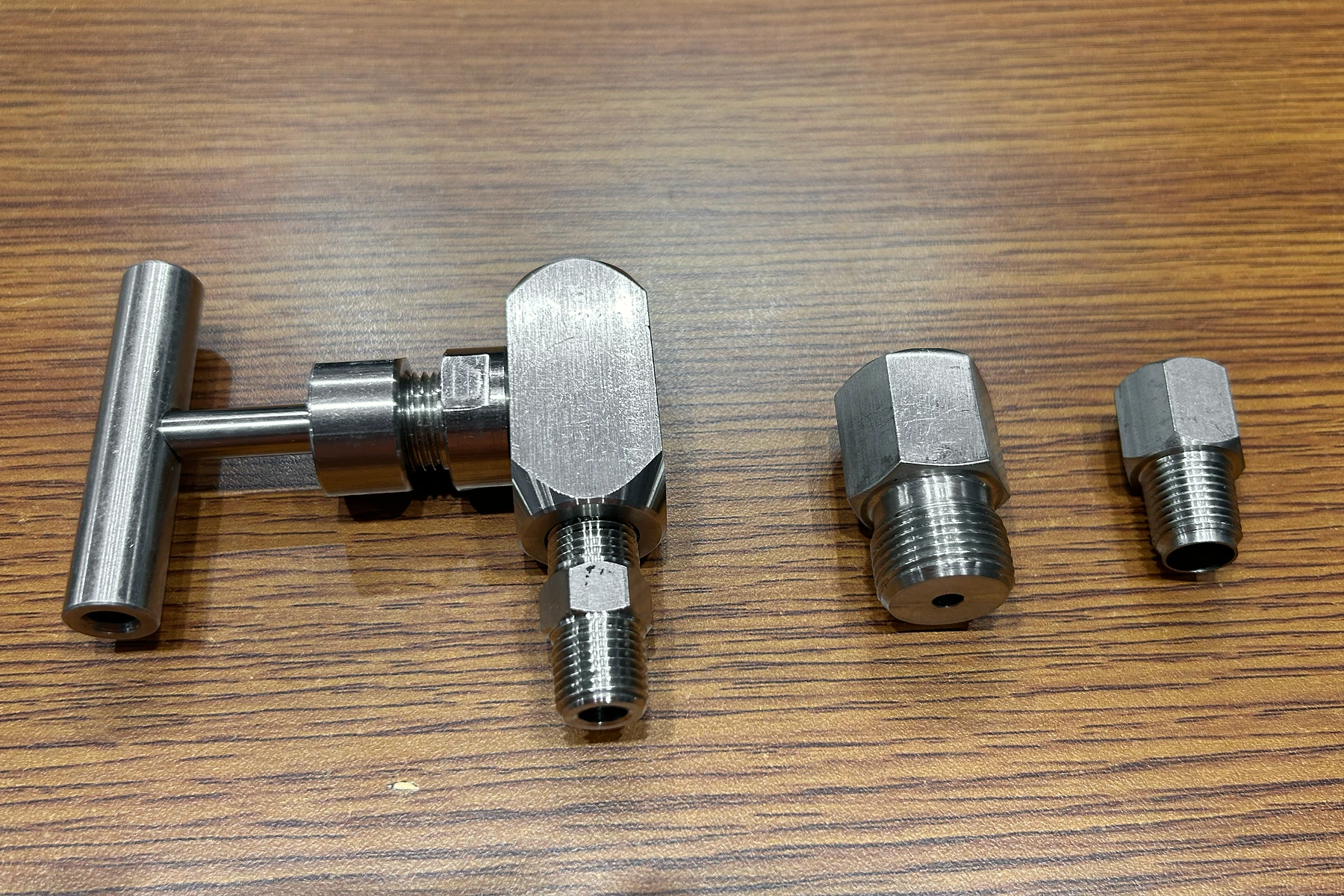 A T-handle valve and two threaded metal fittings on a wooden surface